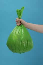 Photo of Woman holding plastic bag full of garbage on light blue background, closeup