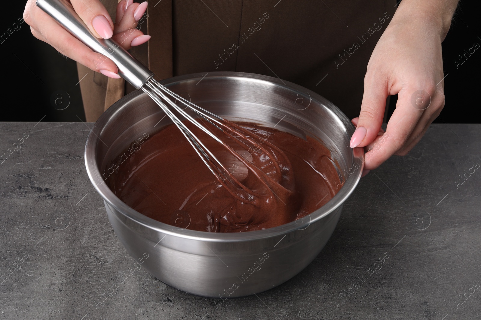 Photo of Woman with whisk mixing chocolate cream at grey table against black background, closeup