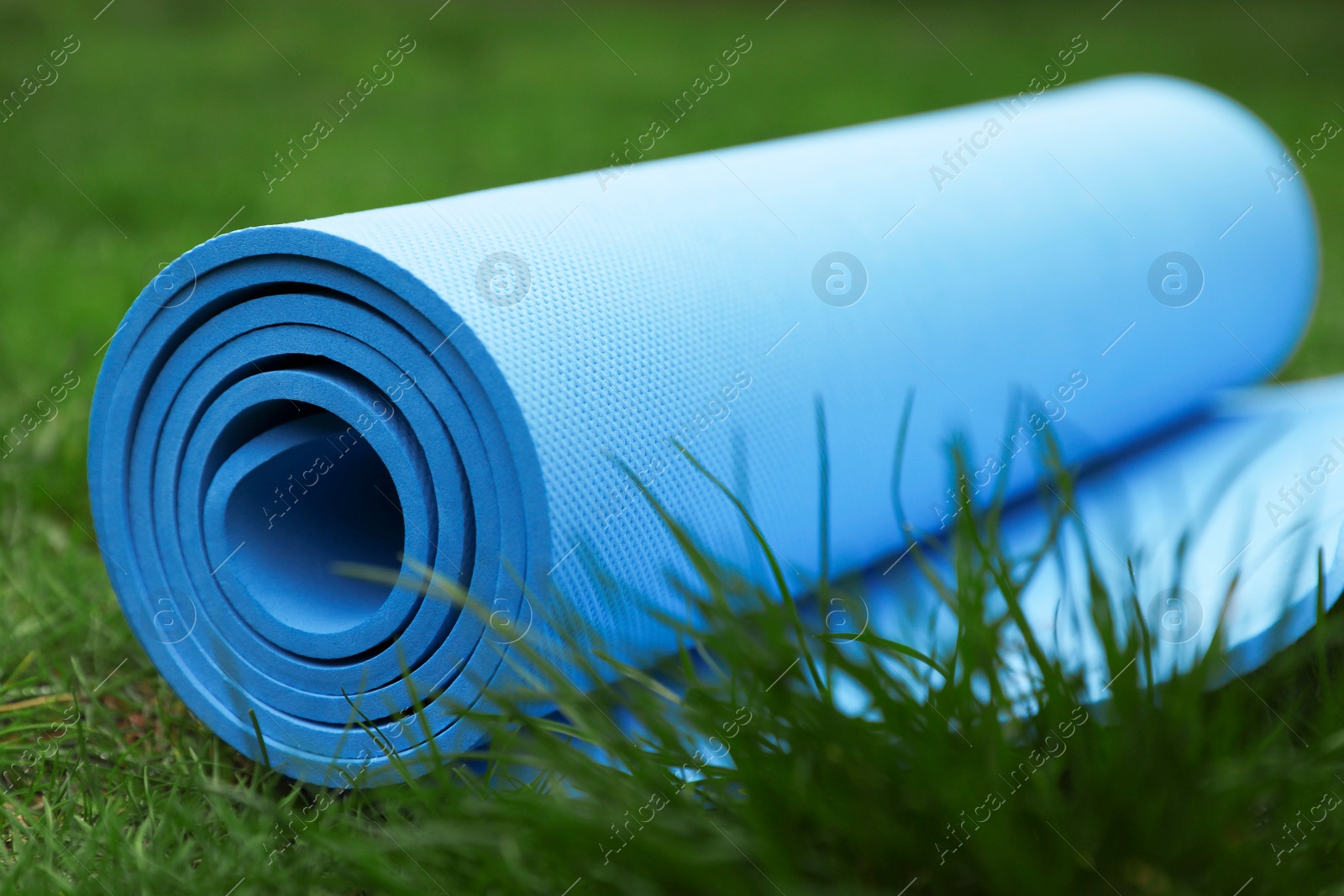 Photo of Bright karemat or fitness mat in fresh green grass outdoors, closeup