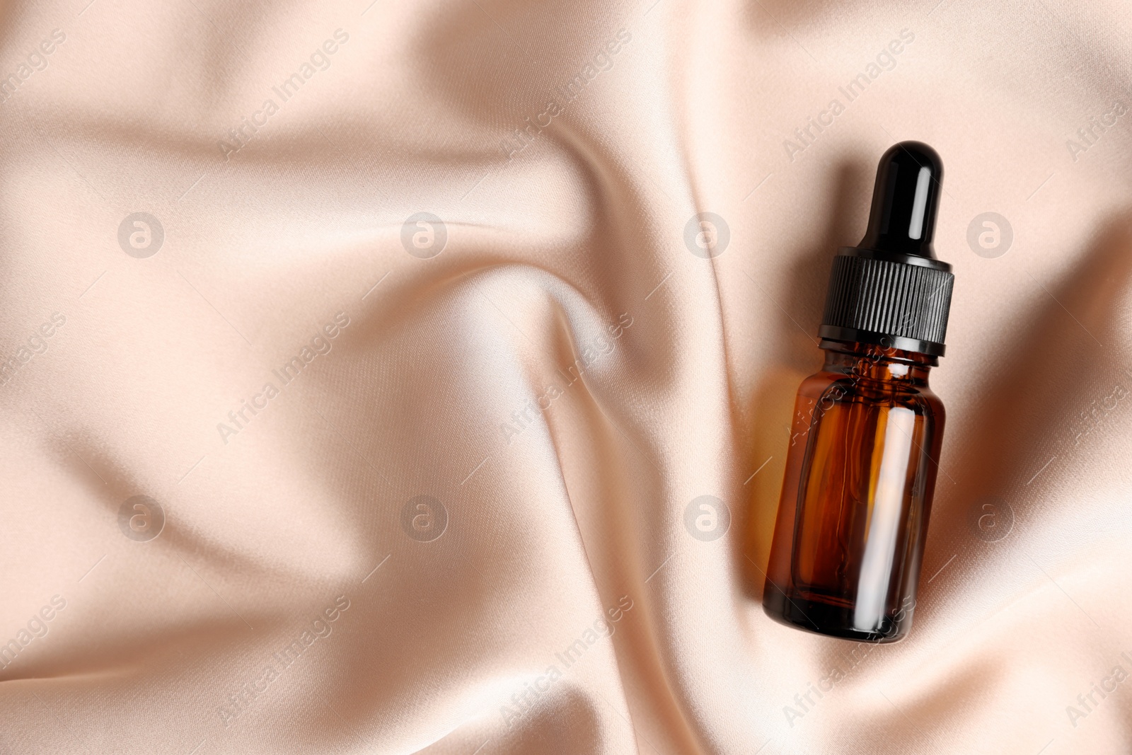 Photo of Bottle of organic cosmetic product on beige silky fabric, top view. Space for text