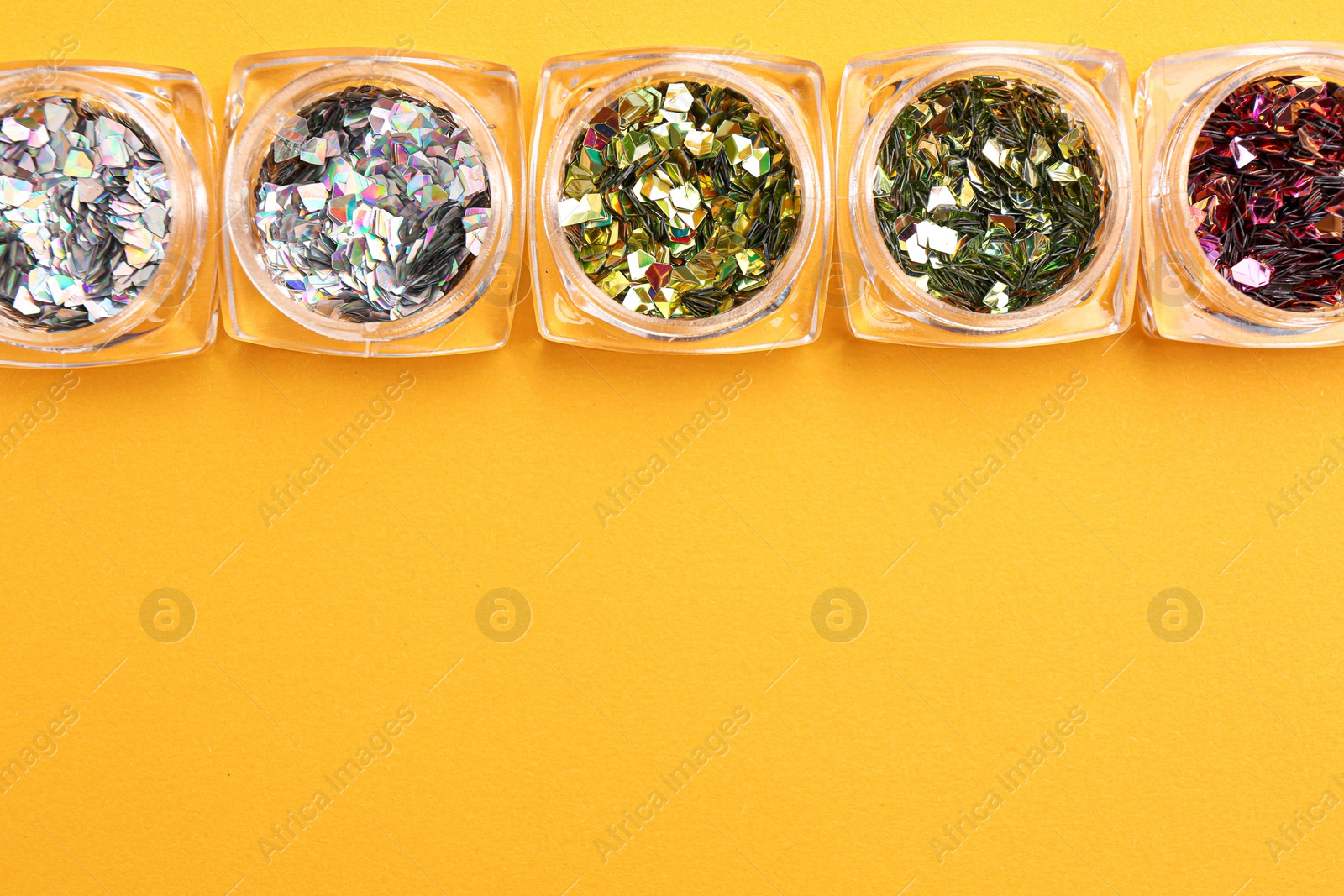 Photo of Jars with colorful shiny glitter on yellow background, flat lay. Space for text