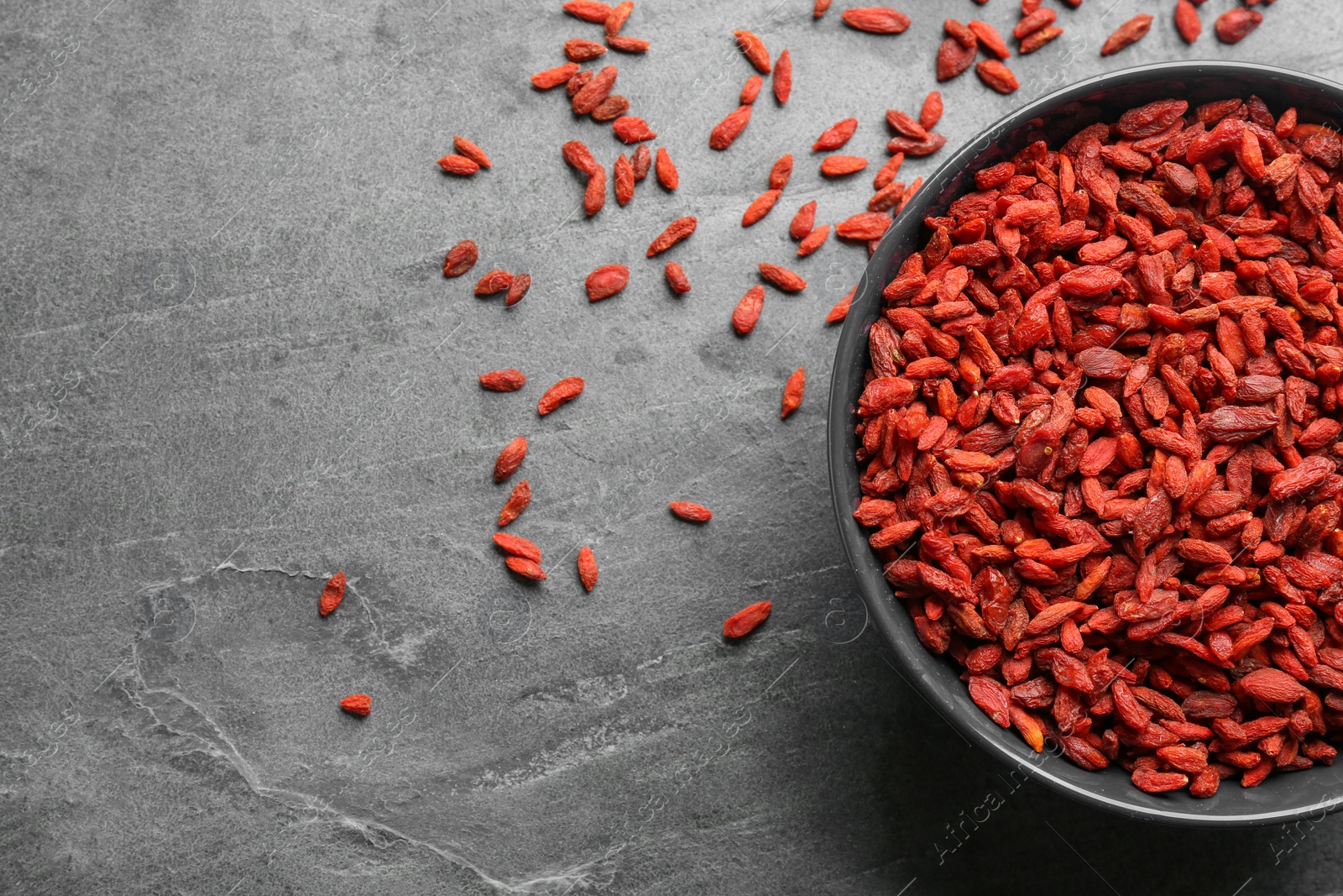 Photo of Bowl of dried goji berries on grey table, top view with space for text. Healthy superfood