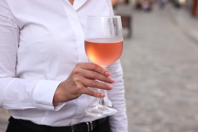 Photo of Woman holding glass of rose wine outdoors, closeup. Space for text