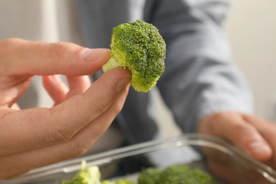 Photo of Man putting fresh broccoli into glass container, closeup. Food storage