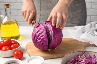 Photo of Woman cutting fresh red cabbage at white wooden table, closeup