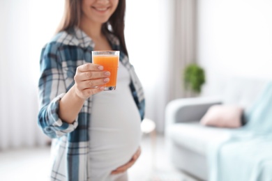 Young pregnant woman holding glass with juice at home