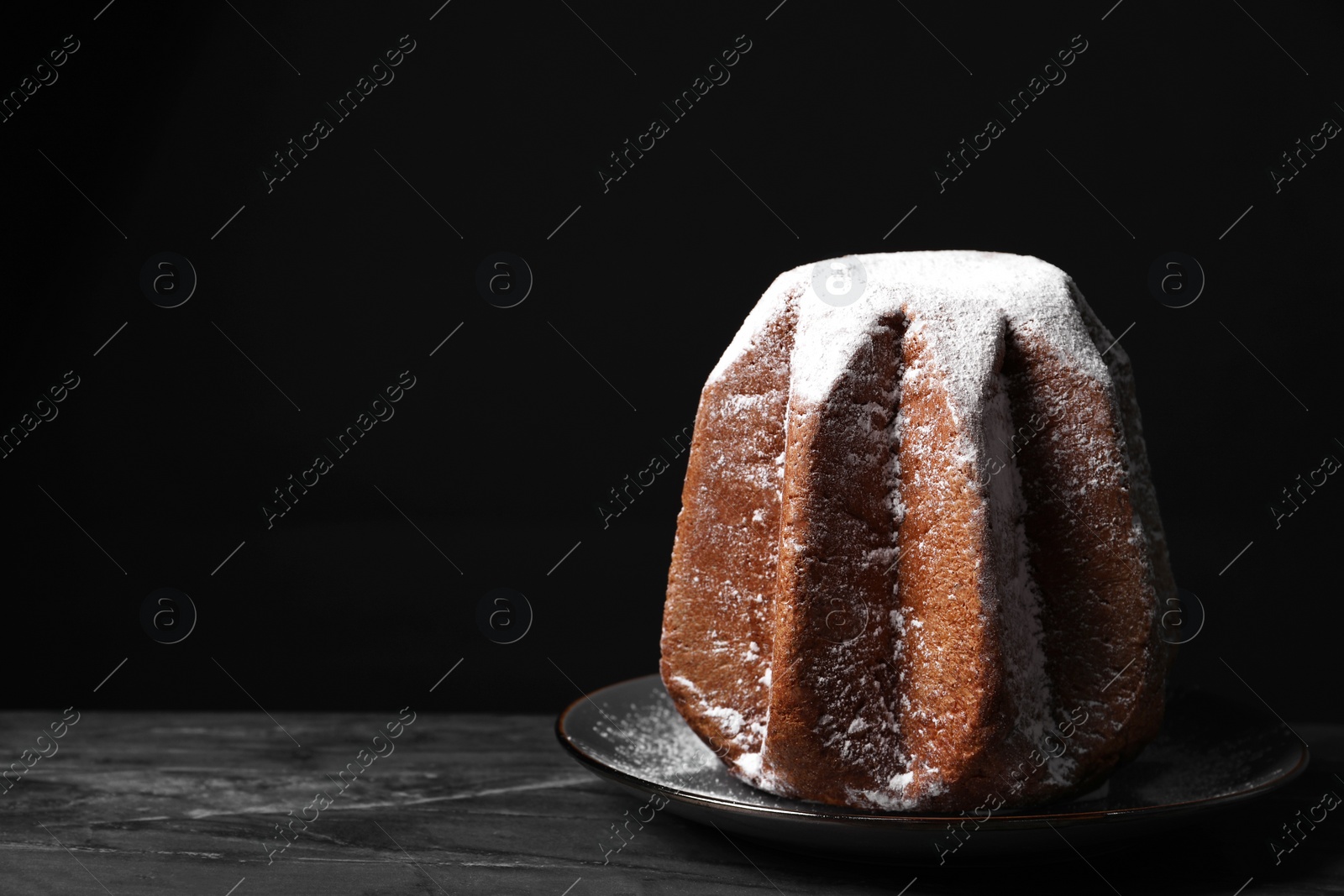 Photo of Delicious Pandoro cake decorated with powdered sugar on dark table, space for text. Traditional Italian pastry