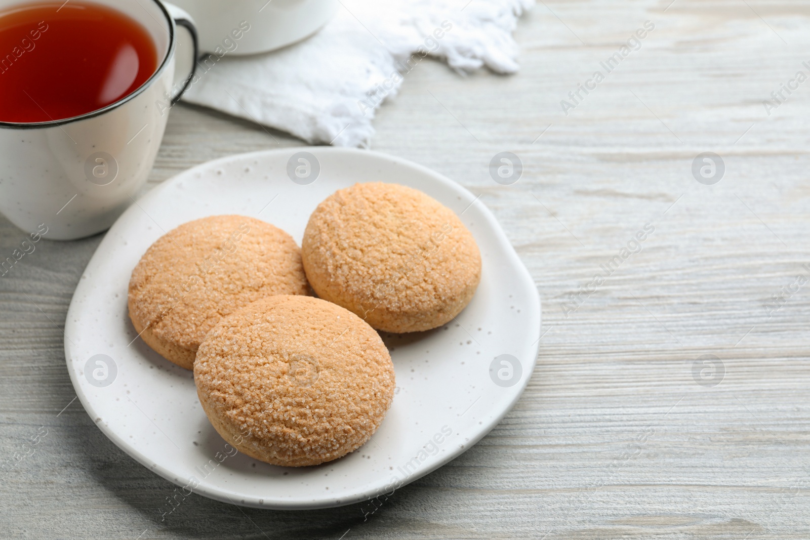 Photo of Delicious sugar cookies and cup of tea on white wooden table, space for text