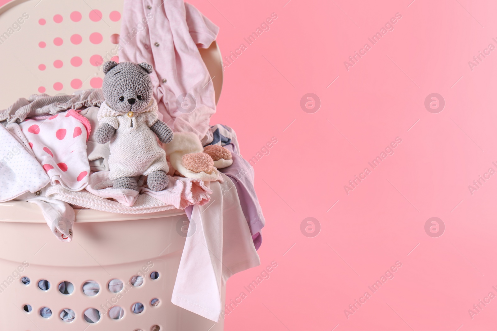 Photo of Laundry basket with baby clothes and soft toy on pink background, closeup. Space for text