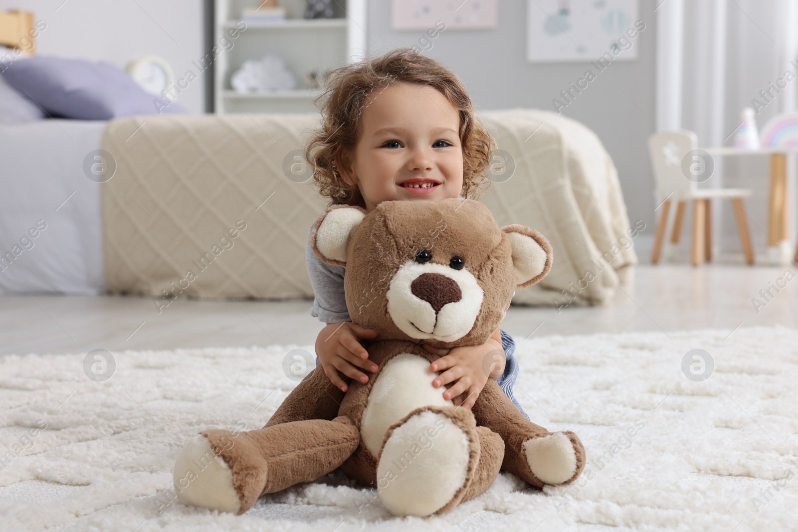 Photo of Cute little girl with teddy bear on floor at home