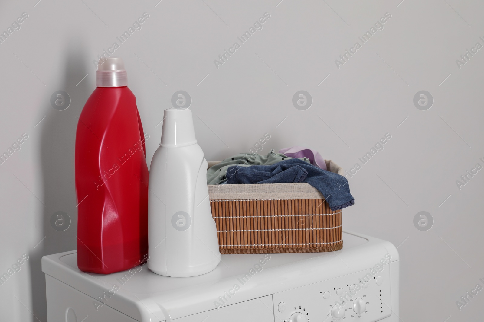 Photo of Baby clothes in wicker basket and laundry detergents on washing machine near light wall, space for text