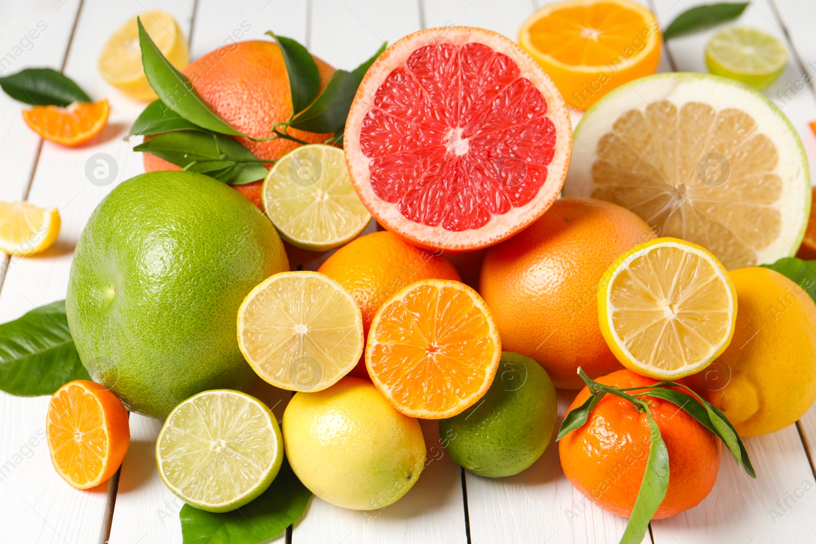 Photo of Different citrus fruits with fresh leaves on white wooden table