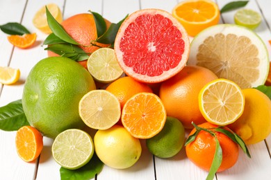 Photo of Different citrus fruits with fresh leaves on white wooden table