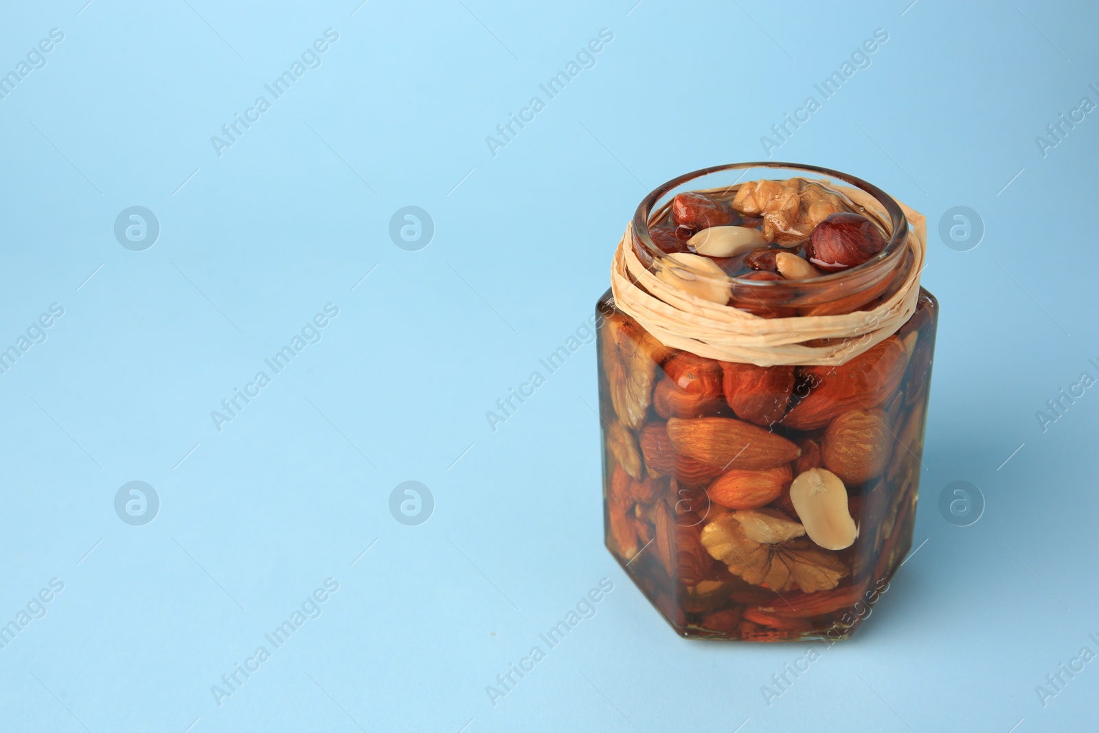 Photo of Jar with different delicious nuts and honey on light blue background. Space for text