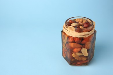 Jar with different delicious nuts and honey on light blue background. Space for text