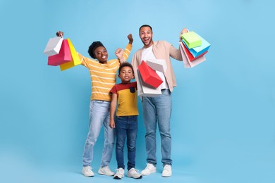 Family shopping. Happy parents and son with colorful bags on light blue background