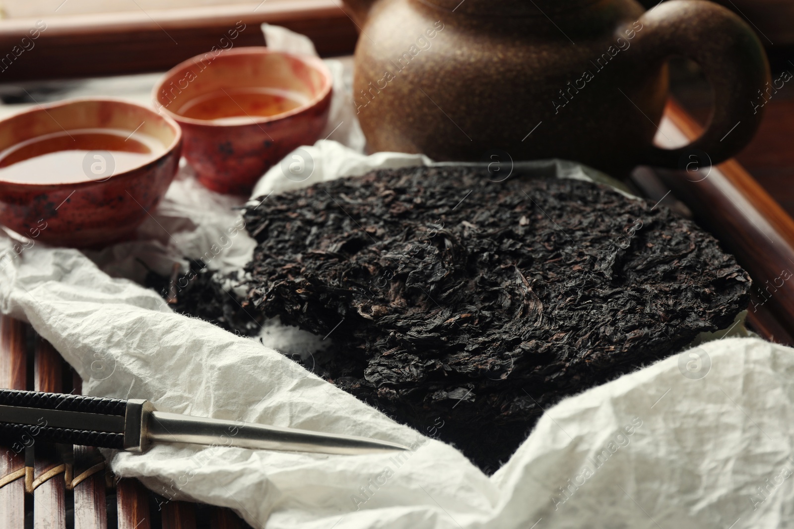 Photo of Broken disc shaped pu-erh tea and knife on wooden tray, closeup