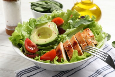 Photo of Eating delicious salad with chicken, cherry tomato and avocado at white table, closeup
