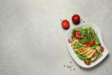 Delicious salad with meat, arugula and vegetables on grey table, flat lay. Space for text