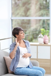 Trendy pregnant woman with tattoo on sofa indoors