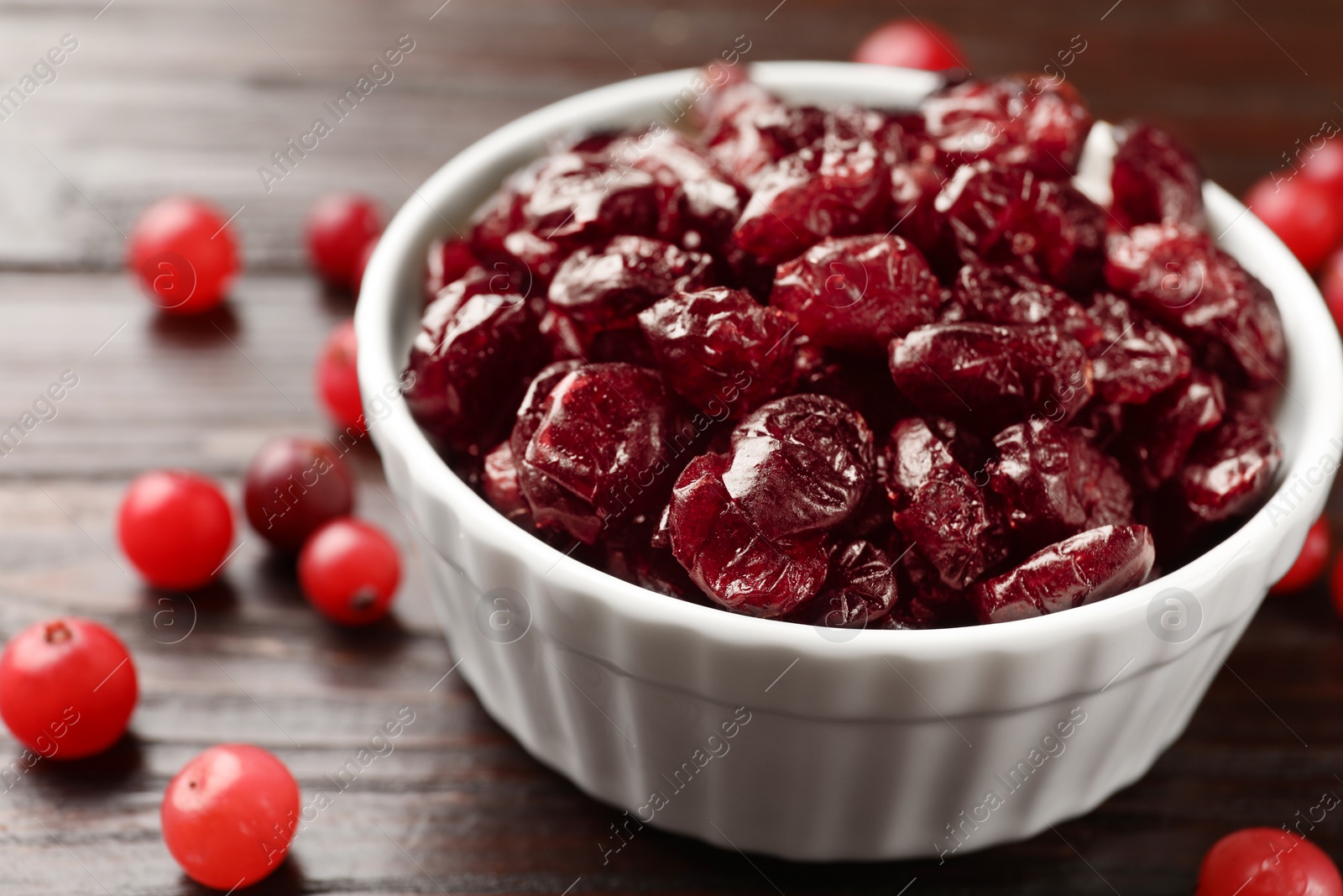 Photo of Tasty dried cranberries in bowl and fresh ones on wooden table, closeup