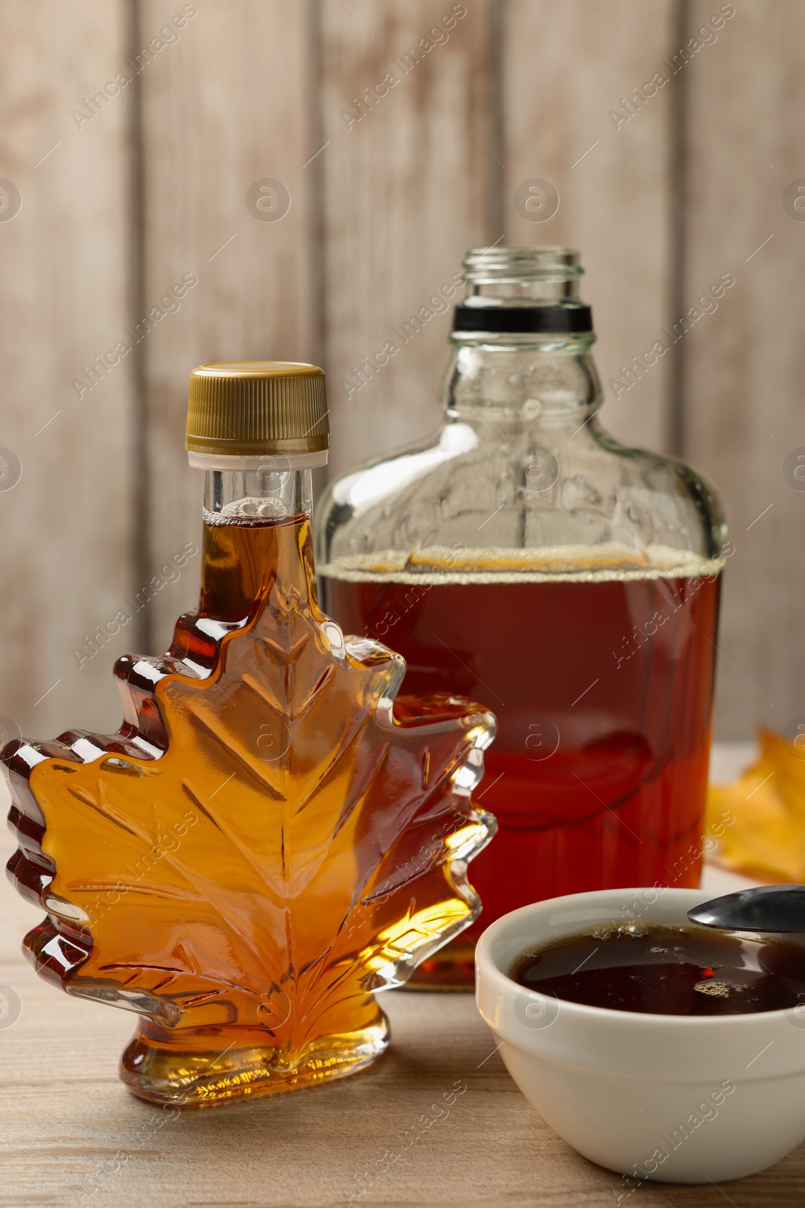 Photo of Bottles and bowl of tasty maple syrup on wooden table