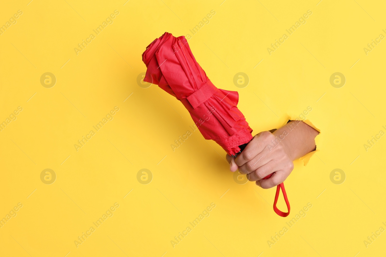 Photo of Woman holding red umbrella through hole in yellow paper, closeup. Space for text