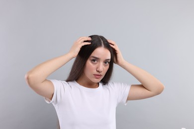 Woman suffering from dandruff problem on grey background