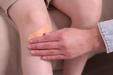 Photo of Woman putting sticking tape onto little boy`s knee on sofa, closeup