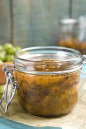 Photo of Jar of delicious gooseberry jam on blue wooden table, closeup