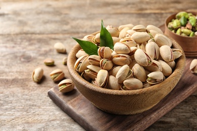Photo of Organic pistachio nuts in bowl on wooden table. Space for text