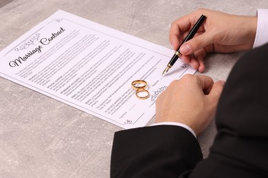 Man signing marriage contract at light grey table, closeup