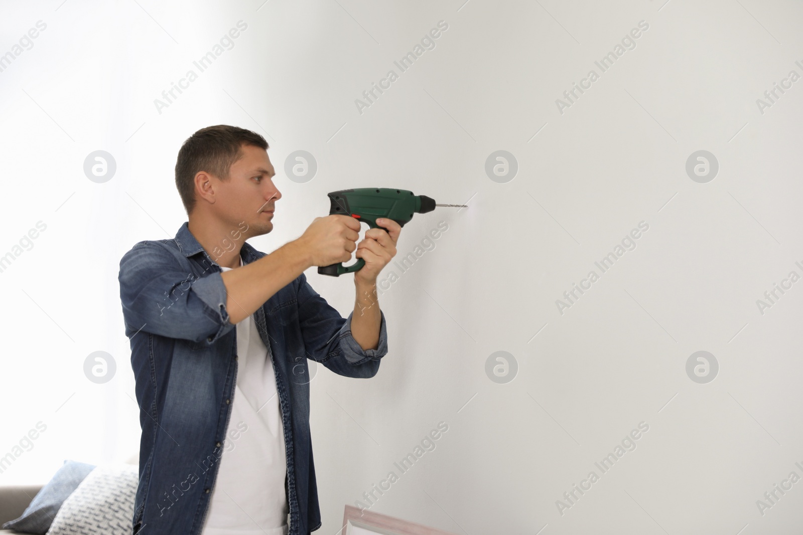 Photo of Man with drill making hole in white wall