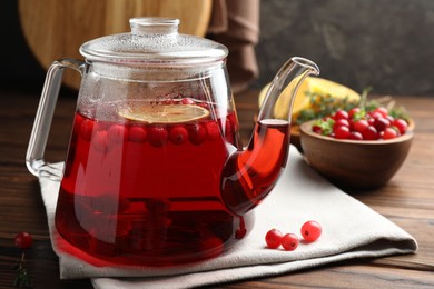 Photo of Tasty hot cranberry tea in teapot and fresh berries on wooden table