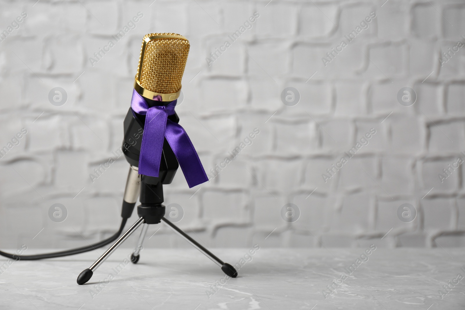 Photo of Microphone with purple awareness ribbon on table against white wall, space for text