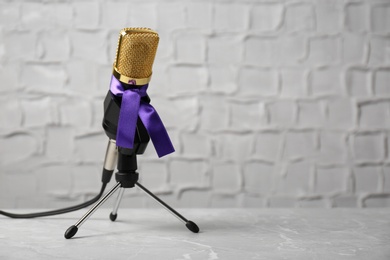 Photo of Microphone with purple awareness ribbon on table against white wall, space for text