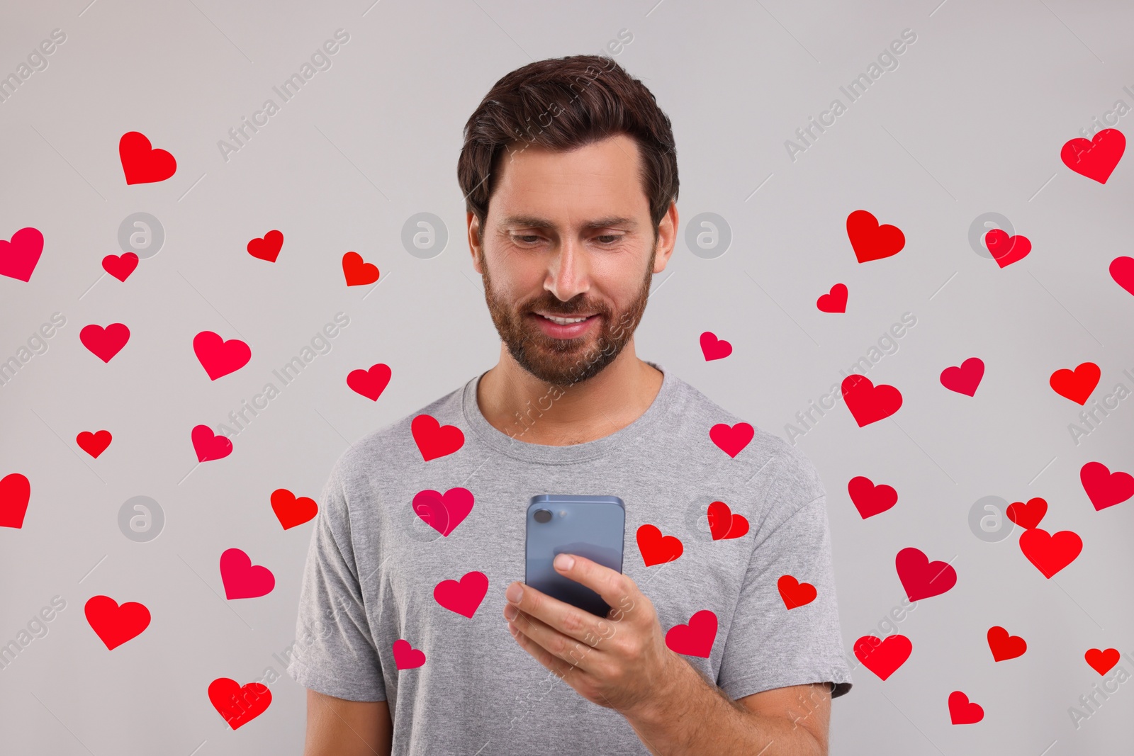 Image of Long distance love. Man chatting with sweetheart via smartphone on grey background. Hearts flying out of device and swirling around him