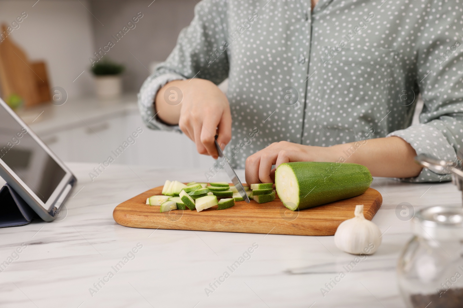 Photo of Cooking process. Woman cutting zucchini at white marble countertop, closeup