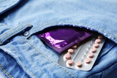 Photo of Purple condom and birth control pills in pocket of jeans, closeup. Safe sex concept