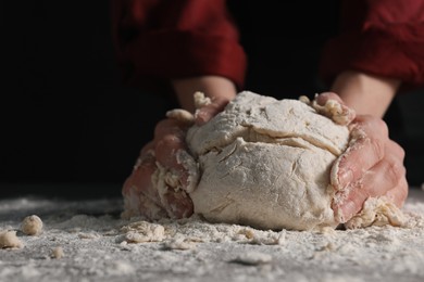 Making bread. Woman kneading dough at table on dark background, closeup. Space for text