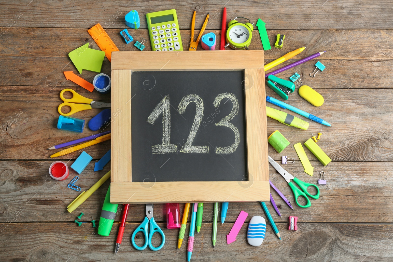 Photo of Small chalkboard with numbers and different school stationery on wooden background, flat lay