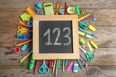 Small chalkboard with numbers and different school stationery on wooden background, flat lay