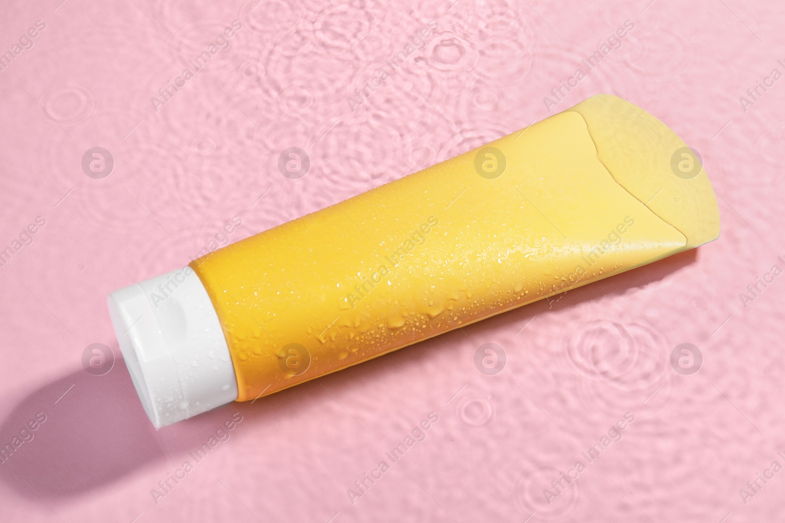 Photo of Tube of face cleansing product in water against pink background