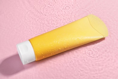 Photo of Tube of face cleansing product in water against pink background