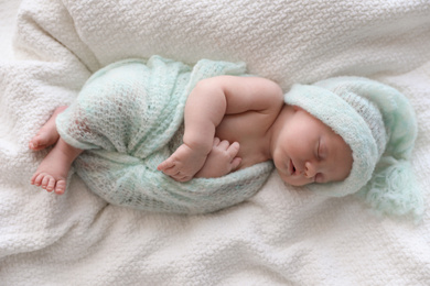 Cute newborn baby in warm hat sleeping on white plaid, top view