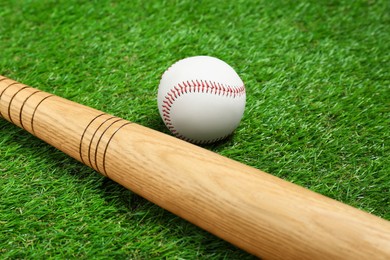 Photo of Wooden baseball bat and ball on green grass, closeup. Sports equipment