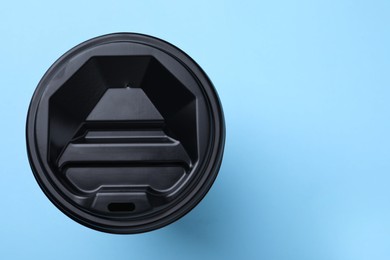 One paper cup with black lid on light blue background, top view with space for text. Coffee to go