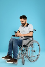 Young man with smartphone in wheelchair on color background