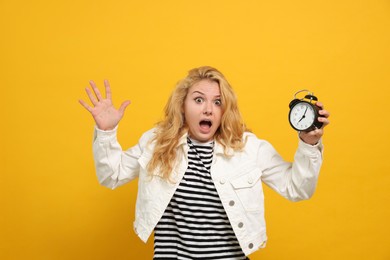 Emotional woman with alarm clock in turmoil over being late on yellow background
