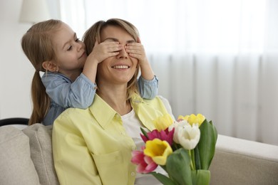 Photo of Little girl surprising her mom with bouquet of tulips at home, space for text. Happy Mother`s Day